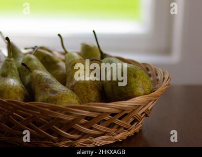 Birnen im Korbkorb auf Holztisch neben dem Fenster Stockfoto