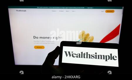 Person, die das Smartphone mit dem Logo des kanadischen Finanzdienstleisters Wealthsimple auf dem Bildschirm vor der Website hält. Konzentrieren Sie sich auf die Telefonanzeige. Stockfoto
