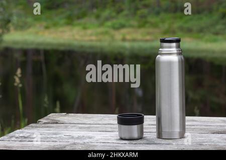 Thermoskanne und Tasse auf Holztisch im Wald Stockfoto