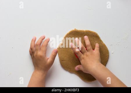 Kinderhände schneiden Formen auf ausgerolltem Lebkuchenteig auf dem weißen Hintergrund Stockfoto