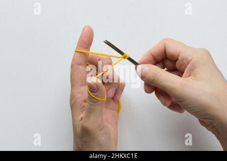 Gießen Sie auf. Stricken. Die Masche auf den Nadeln auf dem weißen Hintergrund festziehen. Draufsicht. Stockfoto