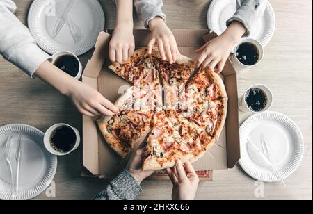 Junge Leute, die heiße Pizza aus dem Karton am Tisch nehmen, Draufsicht. Stockfoto