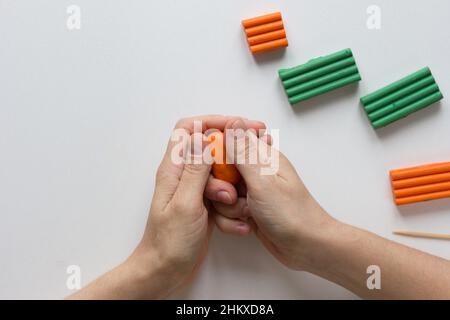 Frau Hände halten orange Stück Fimo, damit es weich und warm, um mit ihm auf dem weißen Hintergrund zu arbeiten Stockfoto