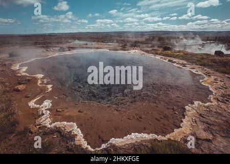 Ein kleiner Teich mit vulkanischem Wasser im Geysir Strokkur auf Island an einem schönen sonnigen Tag. Schwefelrückstand sichtbar am Ufer des Sees. Stockfoto