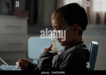 Behandlung zu Hause. Der Junge atmet mit einem Vernebler ein und inhaliert Medikamente in seine Lungen. Selbstbehandlung der Atemwege mit Inhalation. Stockfoto