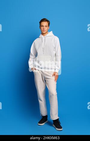 Attraktiver, stilvoller Mann mit weißem Sweatshirt und Sweatshirts, der auf blauem Studiohintergrund steht Stockfoto
