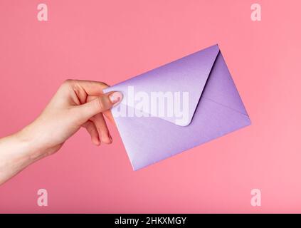 Hand hält lila Umschlag für Valentinstag, Geschenkgutscheine auf rosa Hintergrund. Hochwertige Fotos Stockfoto