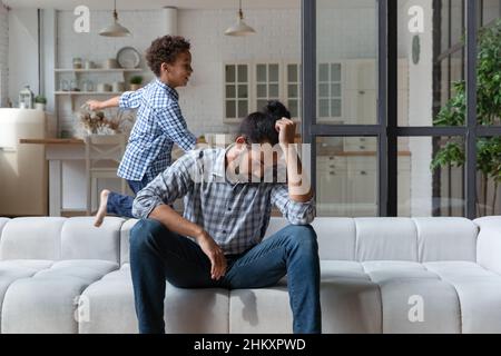 Frustrierter junger afroamerikanischer Vater, der sich des lauten Kindes müde fühlt. Stockfoto