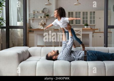 Lächelnder junger afroamerikanischer Vater, der seine Tochter in die Luft hob. Stockfoto