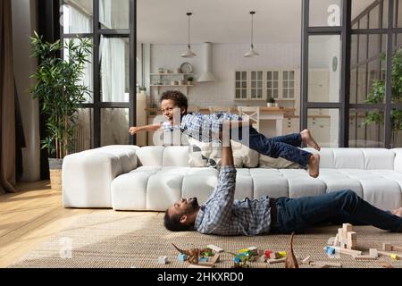 Glücklicher afroamerikanischer Vater, der in der Luft lacht, lachend, kleiner Sohn. Stockfoto