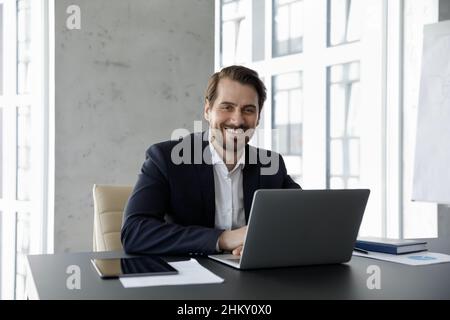 Glücklicher Firmenbesitzer mittleren Alters in formalwear, der am Laptop arbeitete Stockfoto