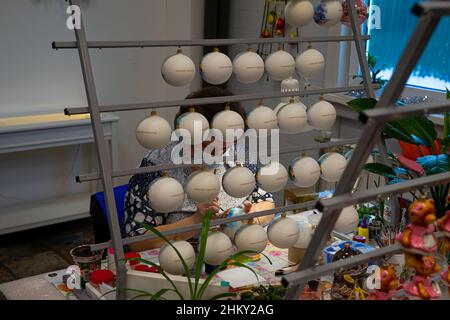 Nischni Nowgorod, Russland. 03. Januar 2022. Frau, die einen Weihnachtsbaumball malt. Fabrik Weihnachtsbaum Spielzeug. Viele Weihnachtsbaumkugeln Stockfoto