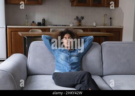 Friedliches afrikanisches Teenager-Mädchen, das sich auf einer gemütlichen weichen Couch ausruht Stockfoto