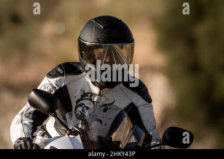 Biker Frau mit schwarzem Helm und Lederjacke läuft auf ihrem Road Motorrad. Unfokussierter Hintergrund Stockfoto