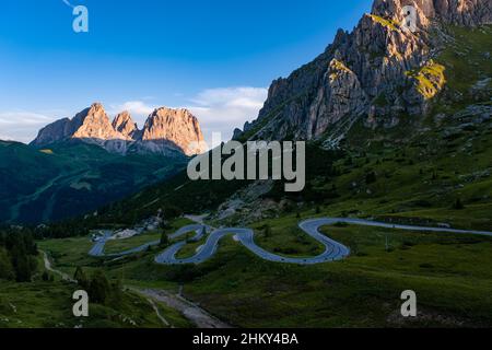 Eine kurvenreiche Straße, die zum Pordoipass führt, die Sellagruppe auf der rechten Seite, Gipfel von Plattkofel, Grohmannspitze und Langkofel in der Ferne. Stockfoto