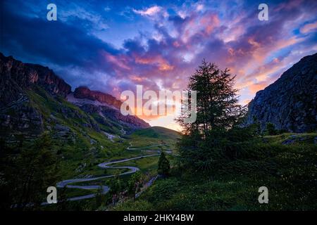 Eine kurvenreiche Straße, die zum Pordoi-Pass führt, Felswände der Sella-Gruppe auf der linken Seite, bei Sonnenaufgang. Stockfoto