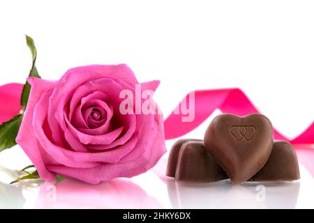 Drei herzförmige Pralinen und rosa Rose auf weißem Hintergrund. Valentinstagskonzept, selektiver Fokus. Stockfoto