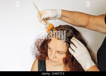 Lange weiße Bürste in den Händen mit Latexhandschuhen bedeckt Putting Färbemittel auf junge Frau Haare auf weißem Hintergrund. Haarfärbung zu Hause. Immer Stockfoto