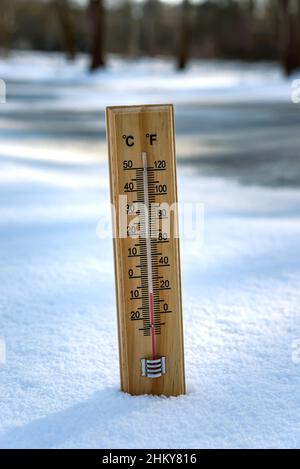 Das Quecksilberthermometer aus Holz, das auf Schnee hängt, weist niedrige Temperaturen auf. Stockfoto