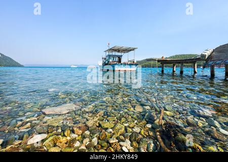 Ein blaues kleines Fischerboot im Meer, das im Hafen mit einem Seil gebunden ist. Klare Sicht auf den Strand von Akbuk Cove (Bucht) in der Provinz Mugla im Südwesten der Türkei. Stockfoto