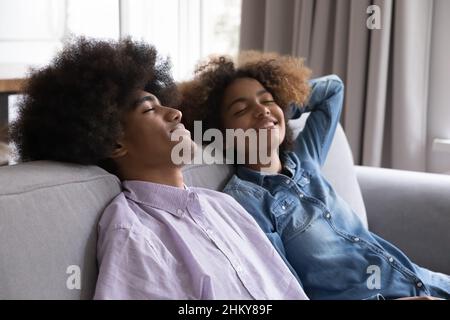 Glückliches Paar von schwarzen Indie-Teenagern, die sich auf der Couch entspannen Stockfoto