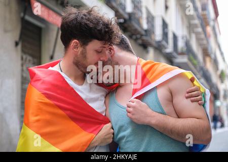 Schwules Paar, umarmt und lächelnd, eingewickelt in eine LGBT-Flagge. Stockfoto