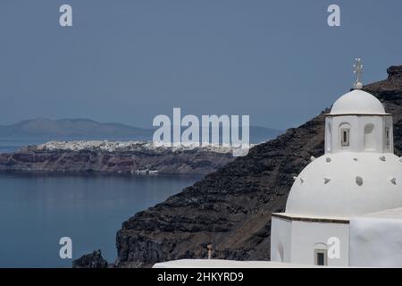 Tolle Aussicht von einer weißgetünchten orthodoxen Kirche und dem berühmten Dorf Oia im Hintergrund Stockfoto