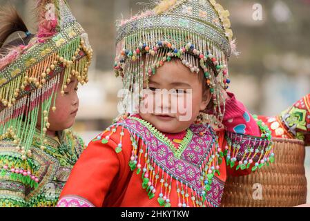 Junge Mädchen, die traditionelle Hmong Stammeskleidung tragen, warten auf Fotos von Touristen auf dem Stadtplatz, Sapa (Sa Pa), Lao Cai, Vietnam Stockfoto