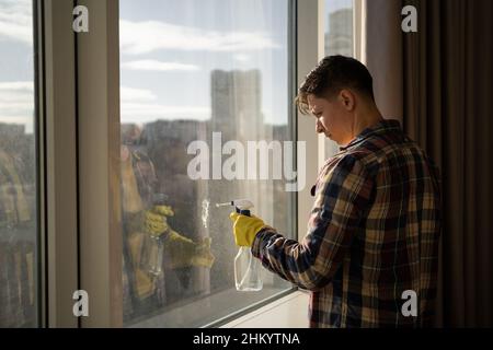 kaukasischer Mann in gelben Gummihandschuhen wäscht Fenster zu Hause. Stockfoto