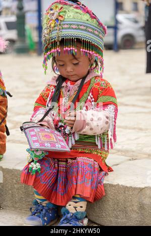 Ein junges Mädchen, das traditionelle Hmong-Stammeskleidung trägt, sammelt Geld für Posen von Touristen in Sapa (Sa Pa), Lao Cai, Vietnam Stockfoto