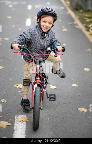 Vater lehrt seinen Sohn, auf dem Radweg im Park Fahrrad zu fahren. Der Vater hält ein Fahrrad und der Sohn sitzt darauf. Stockfoto