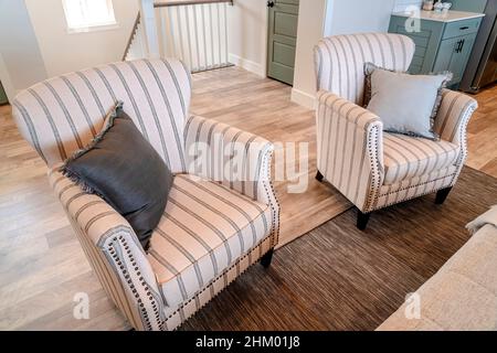 Gestreifte Wohnzimmersessel von zu Hause mit Holzboden und Teppich. Schlafzimmer Tür, Innentreppe und Küche sind im Hintergrund zu sehen. Stockfoto