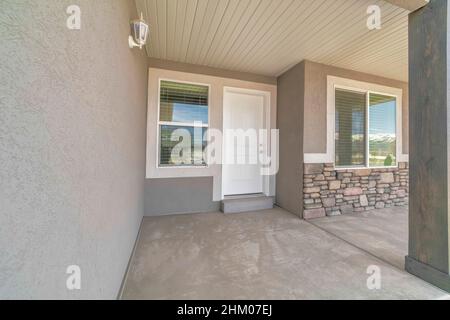 Vordertür außen eines Hauses mit zwei Fenstern und Wandleuchten. Es gibt eine weiße Tür zwischen den Fenstern und ein Steinfurnier-Abstellgleis am Stockfoto