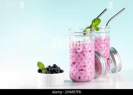 Zwei Gläser Blaubeeren-Smoothie mit Trinkhalmen, Heidelbeeren-Schale auf weiß-türkisfarbenem Hintergrund. Gesundes Getränk ist antiviral, nützlich für die Immunität, reduci Stockfoto