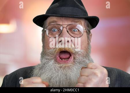Nahaufnahme eines überglücklich alten Mannes, der seine Fäuste auf abstraktem Bokeh-Hintergrund zusammengeballt hat. Menschliche positive Emotionen. Stockfoto