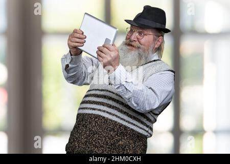 Lustiger älterer Mann mit digitalem Tablet und sieht überrascht aus. Menschen, Technik, Freizeit und Emotionen Konzept. Stockfoto