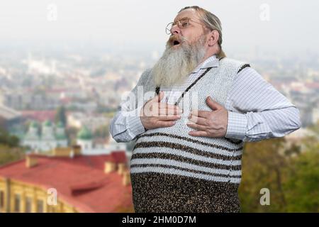 Kranker alter Mann, der an einem Herzinfarkt leidet und im Freien steht. Älterer Mann mit Brustschmerzen. Gesundheitsproblem. Stockfoto