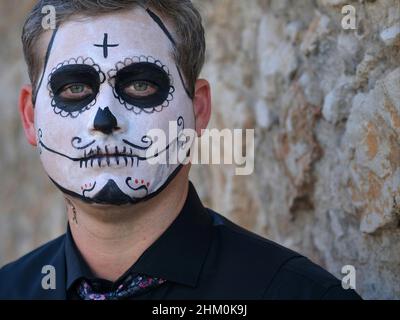 Der junge kaukasische Mann mit gruseliger traditioneller weißer Gesichtsmalerei am Tag der Toten (Día de los Muertos) sieht den Betrachter ernsthaft an. Stockfoto