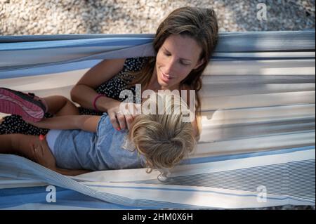 Draufsicht auf eine junge Mutter, die an einem sonnigen Sommertag mit ihrer Kleinkindtochter in einer Hängematte ruht. Stockfoto