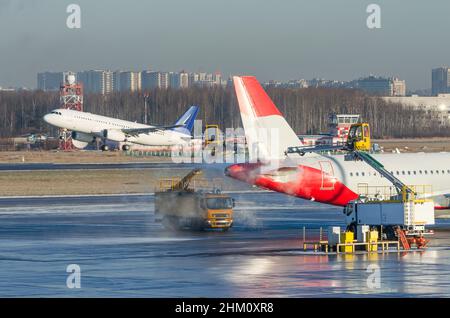 Enteisung des Flugzeugflügels vor dem Flug. Frostiger Wintertag am Flughafen und ein Flugzeug, das im Hintergrund abfliegt Stockfoto