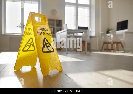 Gelbes „Vorsicht, nasser Boden“-Schild, das vom Hausmeisterdienst in ein sauberes, leeres Büro gebracht wird Stockfoto