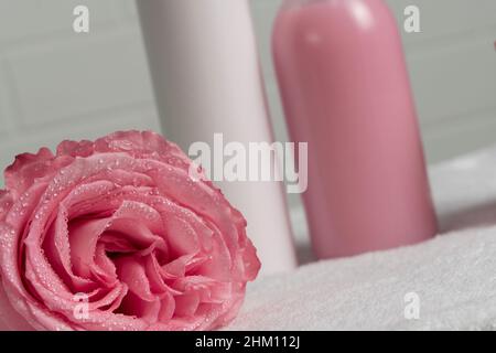 Rosa Rose auf dem Hintergrund von Kosmetikgläsern. Schönheit, Selbstversorgung. Nahaufnahme der Blumen. Wassertropfen auf die Blütenblätter einer Blume. Rosa Hintergrund, tendernes Stockfoto