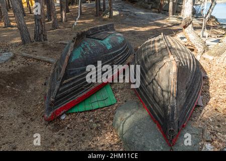 Alte Boote liegen kopfüber am Ufer. Zwei Holzboote ohne Ruder liegen in einem Nadelwald in der Nähe eines Bergsees. Alte, verblasste Boote sind auf dem Schiff Stockfoto