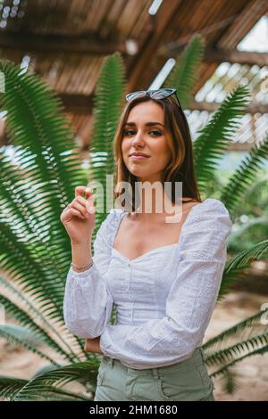 Porträt eines Teenagers, das eine Sonnenbrille trägt. Sie posiert mit einer grünen Handfläche im Hintergrund. Stockfoto