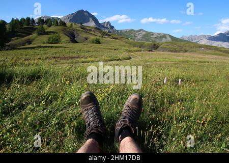 Die Beine und Wanderschuhe eines Wanderers, der im Juli auf dem Gras ruht (Col des Champs, Parc du Mercantour, Alpes-de-Haute-Provence, Frankreich). Stockfoto