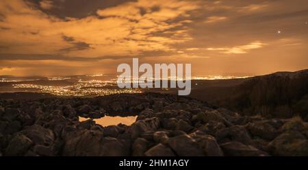 Blick von einem Felsen auf eine beleuchtete Stadt nach Sonnenuntergang Stockfoto