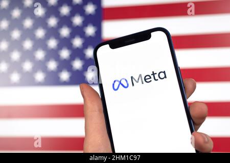 Meta-Logo und amerikanische Flagge auf dem Hintergrund. Facebook Metaverse und USA. Hand mit Mobiltelefon Stockfoto