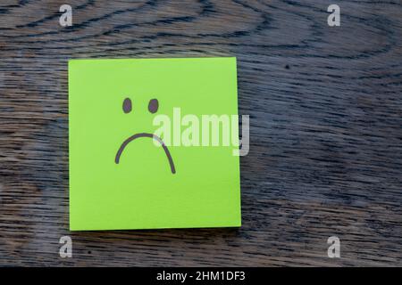 Trauriges Gesicht, handgezeichnet auf Post-it-Notiz, isoliert auf rustikalem Holzhintergrund. Depression, Angst, Einsamkeit, psychische Gesundheit Konzept. Stockfoto