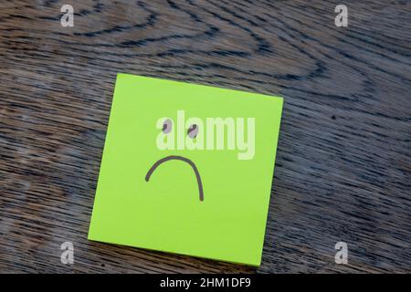 Trauriges Gesicht, handgezeichnet auf Post-it-Notiz, isoliert auf rustikalem Holzhintergrund. Depression, Angst, Einsamkeit, psychische Gesundheit Konzept. Stockfoto