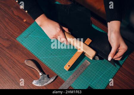 Tanner Frau schneidet Lederwaren in der Werkstatt. Arbeitsprozess des Lederhandwerks. Stockfoto